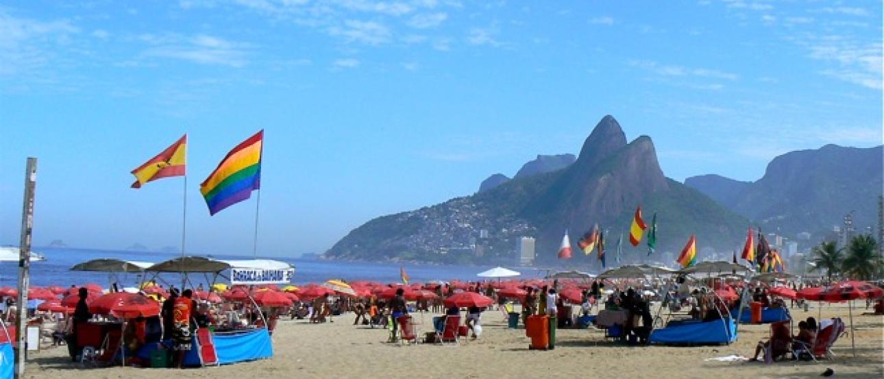 Crowded Rio de Janeiro beach with colorful flags and umbrellas under a blue sky. This alt text was added with Al; accuracy may vary.