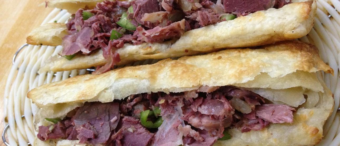 Two stacked flatbread sandwiches with sliced meat and herbs. This alt text was added with Al; accuracy may vary.