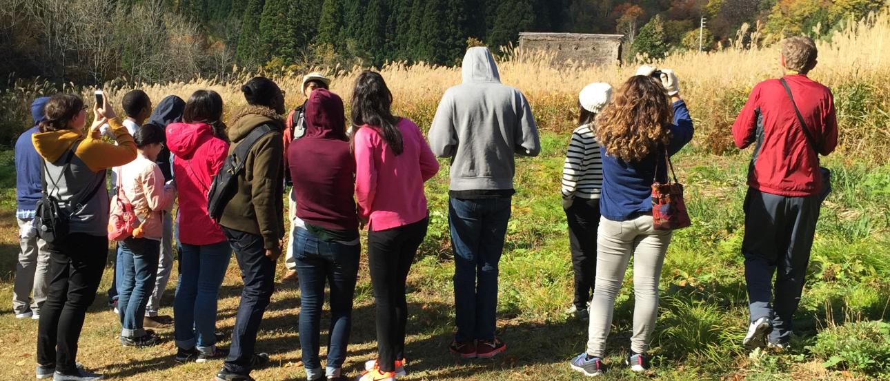 Group of people gathered in a field with mountains in the background, under a clear blue sky. This alt text was added with Al; accuracy may vary.