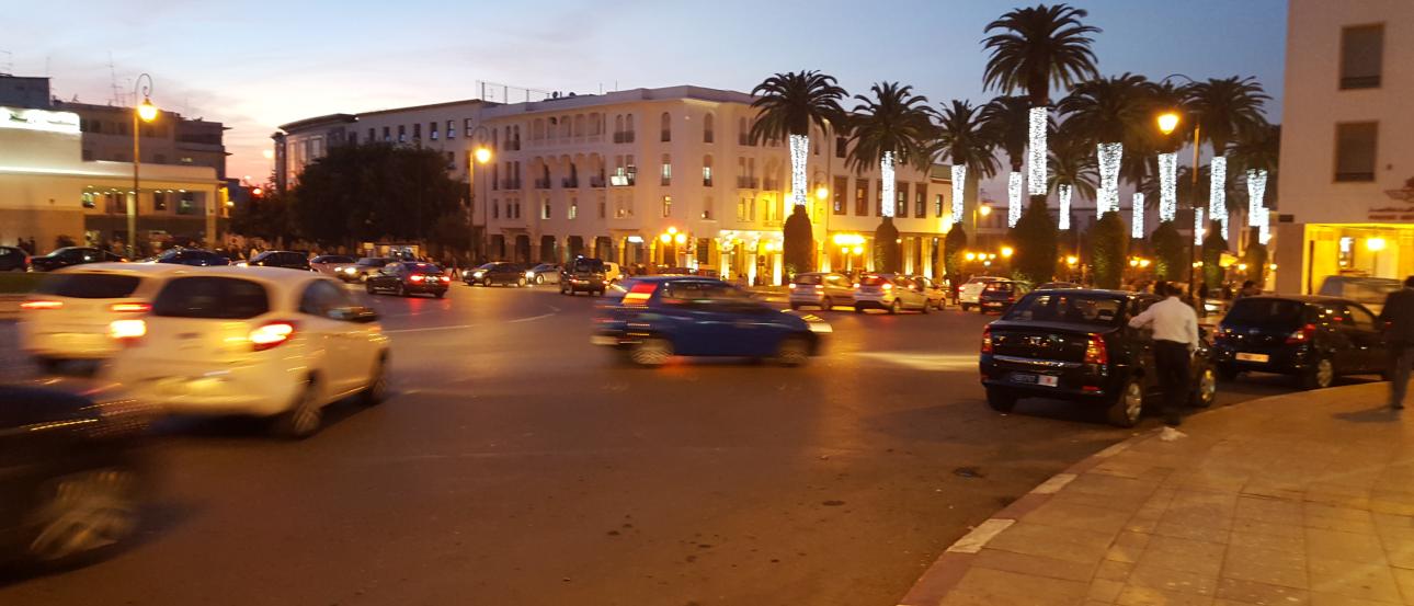Clay pots and tagines displayed outdoors under palm trees at a market.

Dimly lit shop filled with hanging lamps and decorative items.

Five friends smiling by the waterfront on a sunny day.

Metal container with cooked food next to a small bowl on a table.

Cars drive around a city square with lit buildings and palm trees at dusk. This alt text was added with Al; accuracy may vary.