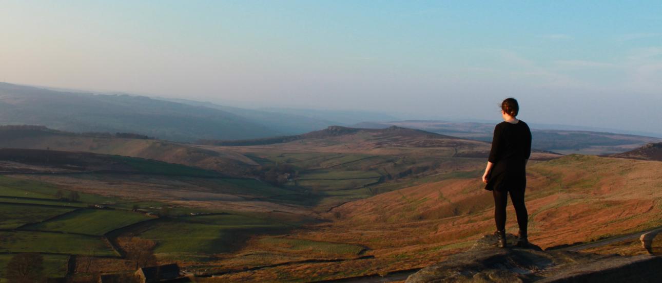 Standing on a hill, person gazes over vast, rolling landscape at sunset. This alt text was added with Al; accuracy may vary.