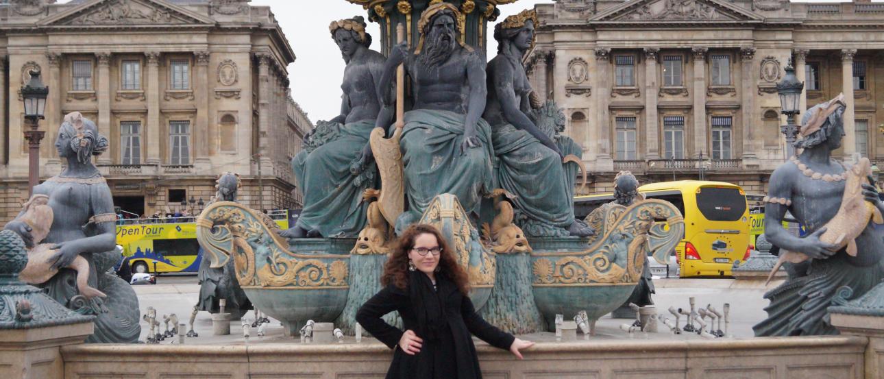 Red rooftops of a European town under a hazy sky.

Neoclassical building with columns and ivy, against a mountain backdrop.

Person poses in front of ornate fountain with statues at a plaza. This alt text was added with Al; accuracy may vary.