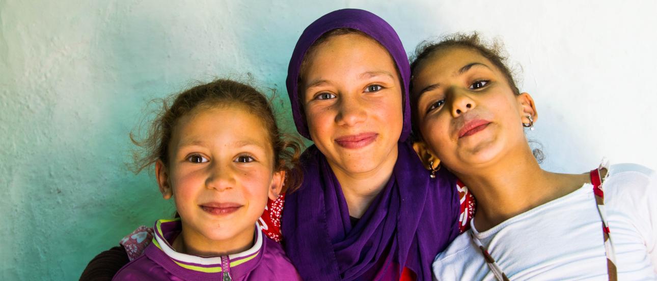 A diverse group of friends smiling by a riverside, with historic buildings in the background. This alt text was added with Al; accuracy may vary.