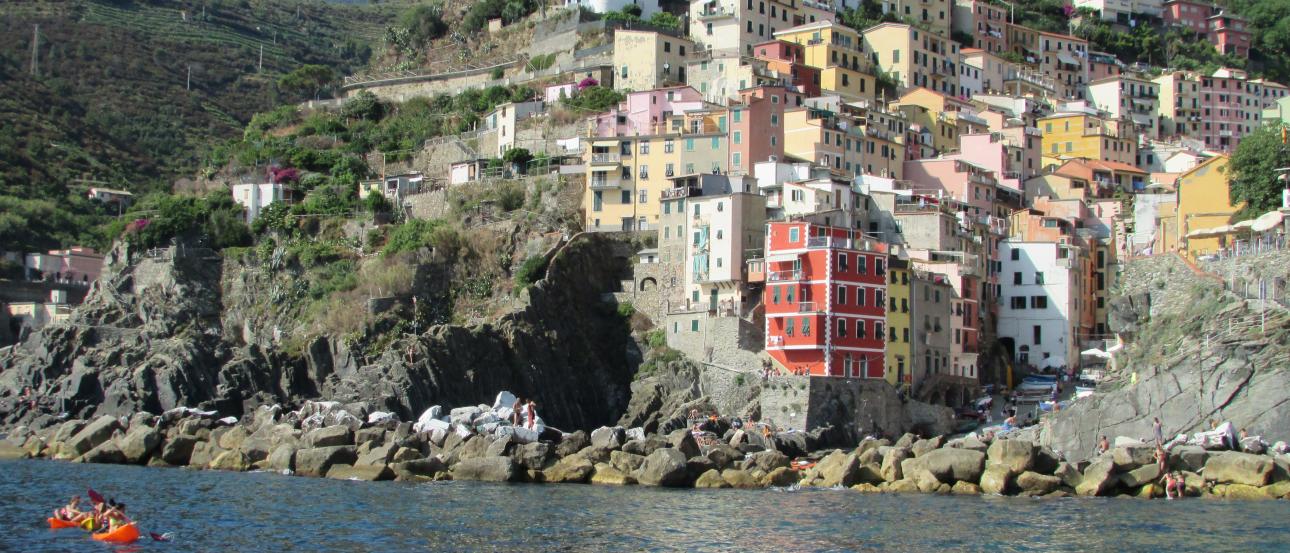 Colorful hillside village by the sea, with cliffs and a small boat. This alt text was added with Al; accuracy may vary.