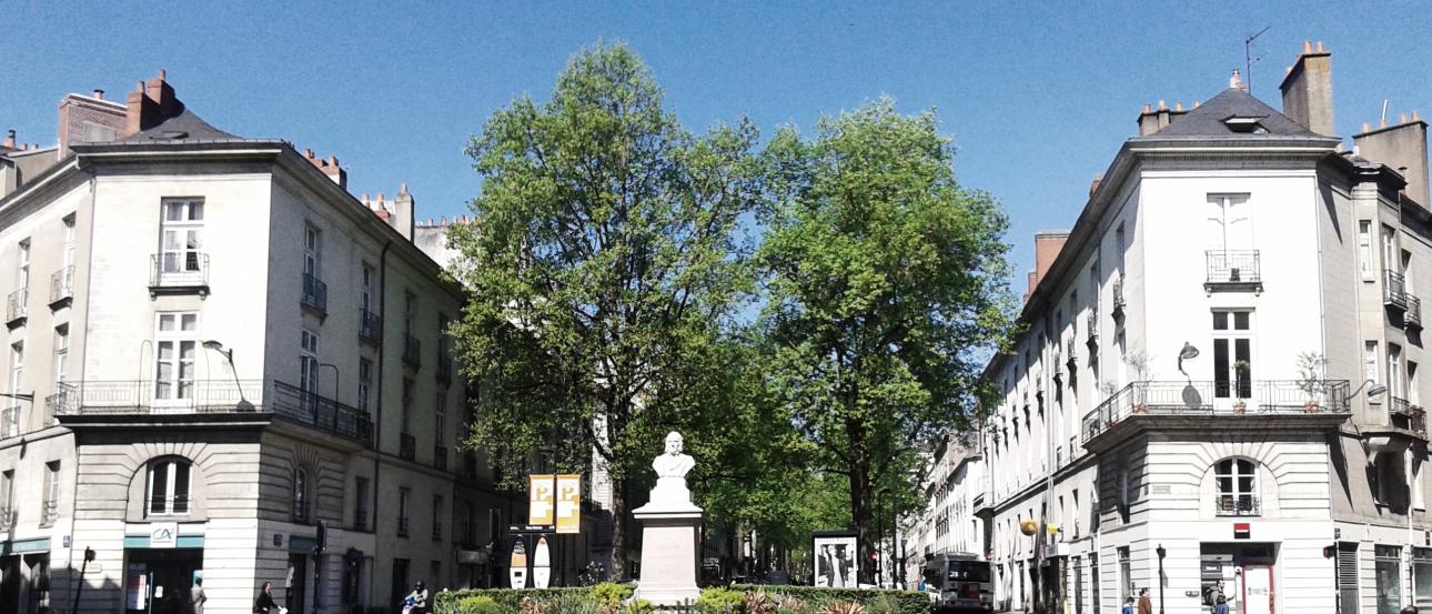 Spacious city square with people walking, sunlit buildings, and a clear sky. This alt text was added with Al; accuracy may vary.