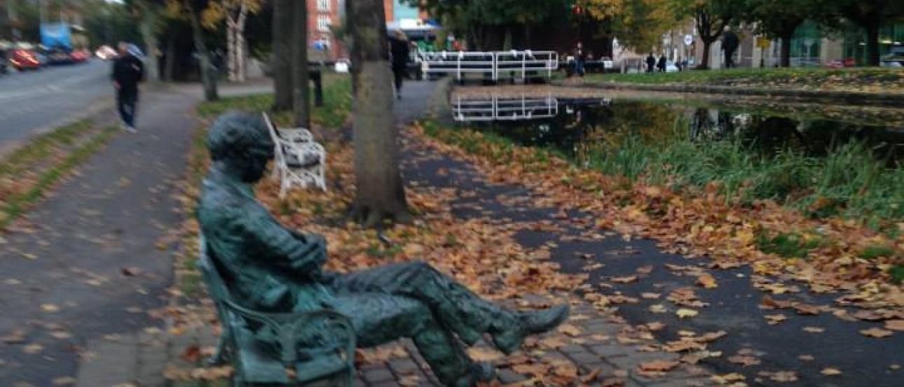 Night view of Sagrada Familia with illuminated spires and cranes. 

Park bench statue, surrounded by autumn leaves, with trees lining a path. This alt text was added with Al; accuracy may vary.