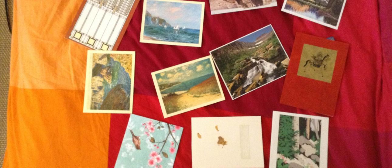 Postcards scattered on a colorful bedspread, featuring landscapes and art. This alt text was added with Al; accuracy may vary.