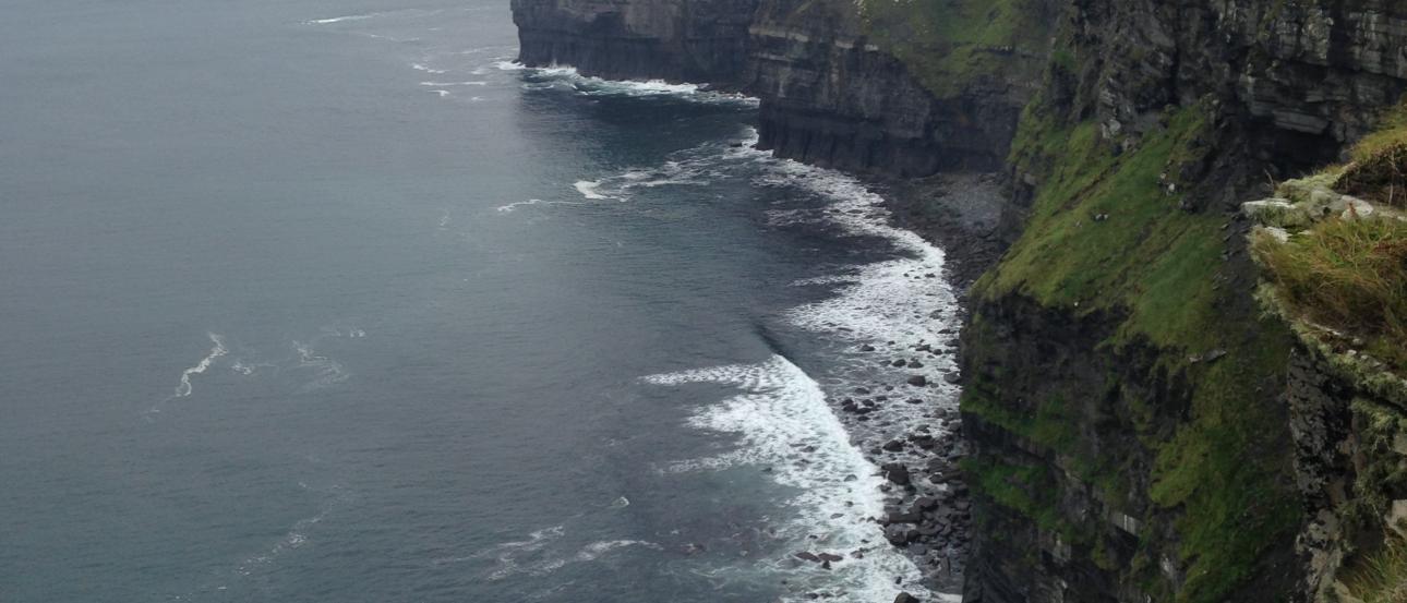Cliffs with ocean waves below, under a cloudy sky. This alt text was added with Al; accuracy may vary.