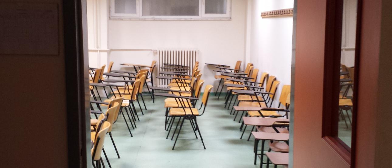 Classroom with rows of empty desks and chairs, viewed through an open door. This alt text was added with Al; accuracy may vary.