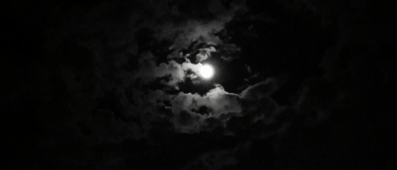 River winding through grassy hills under a cloudy sky.

Moon partially obscured by dark clouds in the night sky. This alt text was added with Al; accuracy may vary.
