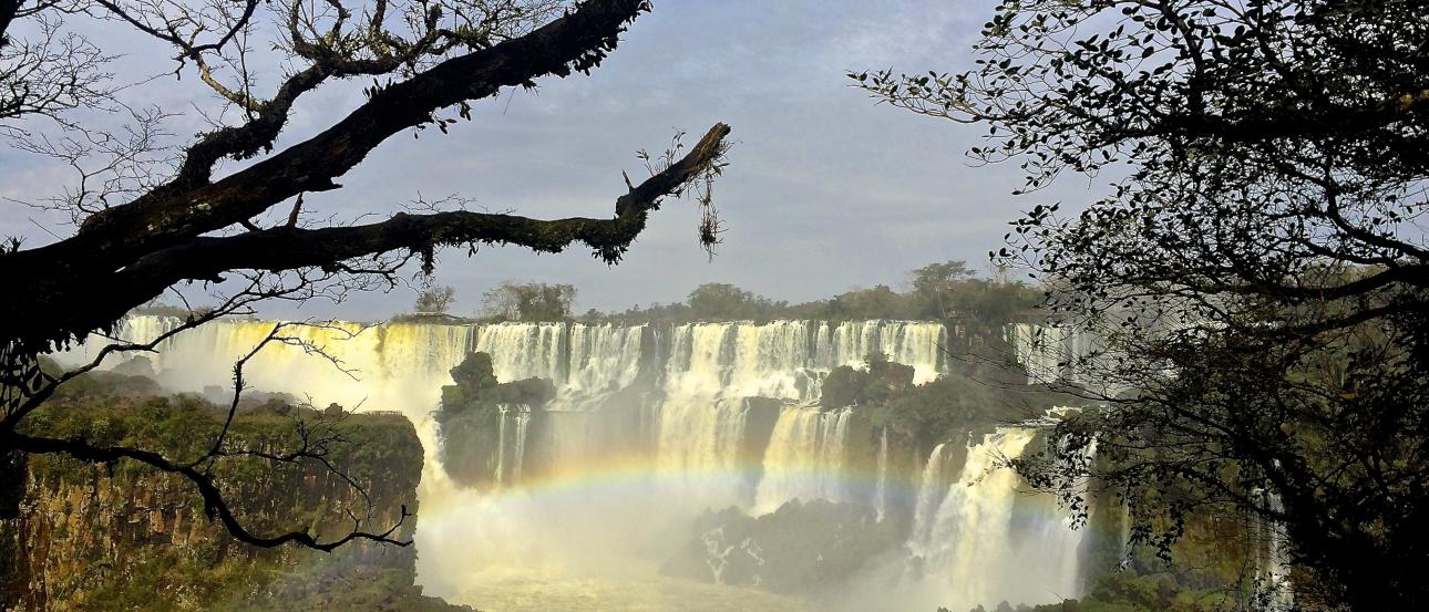 Waterfall framed by trees with a rainbow in the mist. This alt text was added with Al; accuracy may vary.