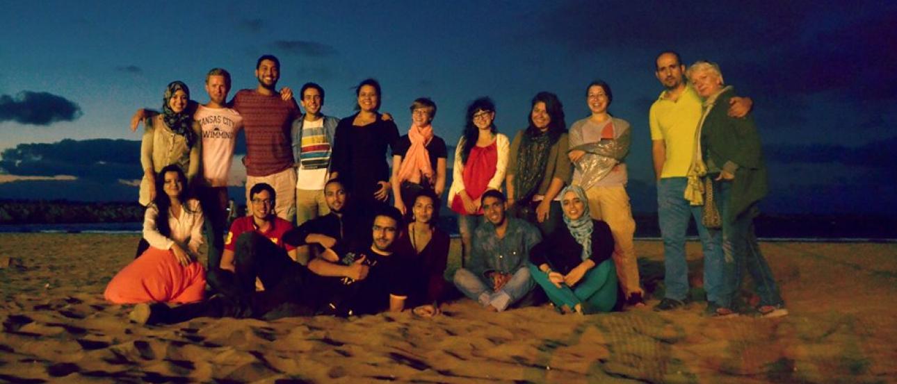 Group of people posing on a beach at dusk. This alt text was added with Al; accuracy may vary.