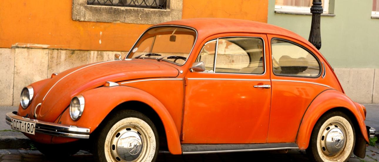 Orange vintage Volkswagen Beetle parked by an orange wall. This alt text was added with Al; accuracy may vary.