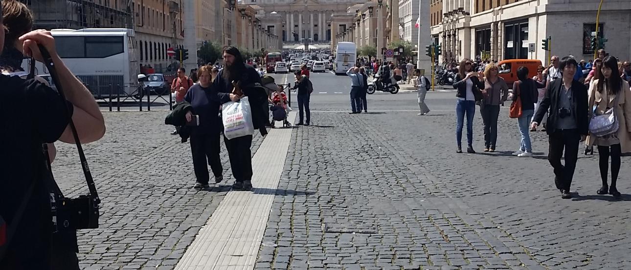 Wide street view towards St. Peter's Basilica, Rome, with people walking. This alt text was added with Al; accuracy may vary.