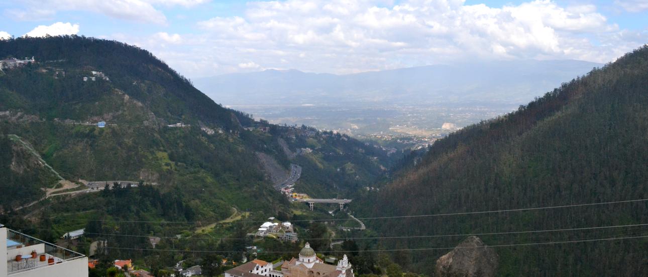 Mountain valley view with hills, clouds, and distant landscape. This alt text was added with Al; accuracy may vary.