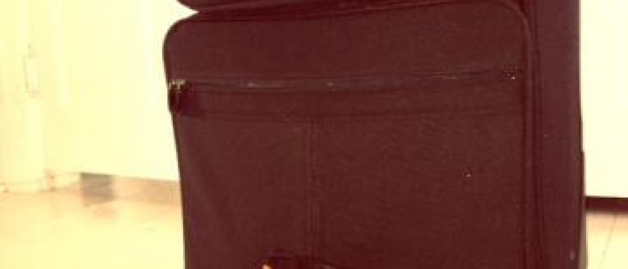 Orange hiking boots beside a black suitcase on a light-colored floor. This alt text was added with Al; accuracy may vary.