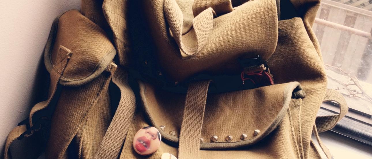 Backpack with buttons on windowsill, wooden fence view. This alt text was added with Al; accuracy may vary.