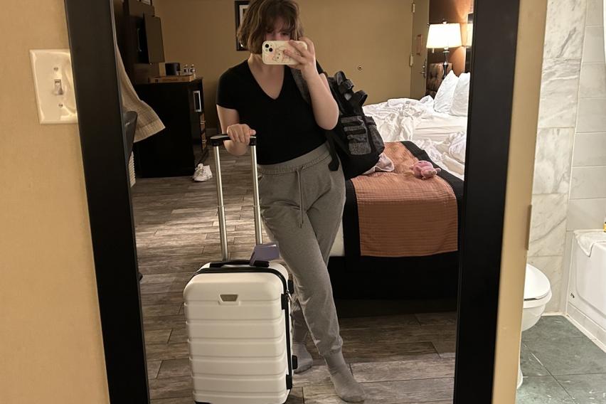 A photo of me in the mirror holding my suitcase and personal item in my hotel room.