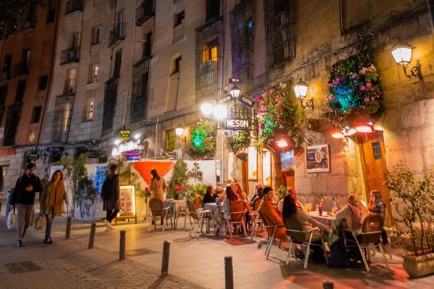 People eat outside at night on a street lined with lights in Madrid, Spain.