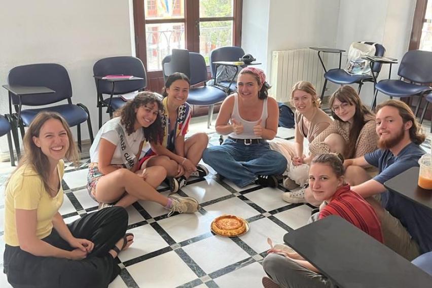 Spanish class sitting in a circle on the floor around a cheesecake.