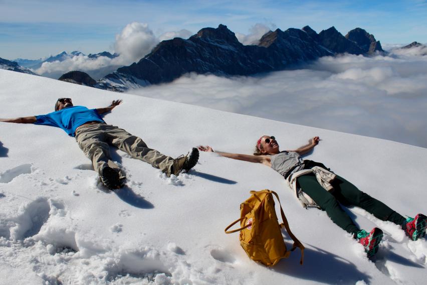 students laying in snow making angels with mountains in the background