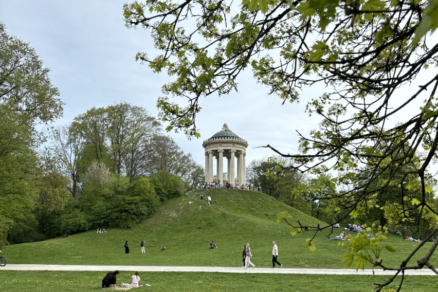 A photo of the english gardens with a big, white, circular building with pillars sitting on top of a tall hill 