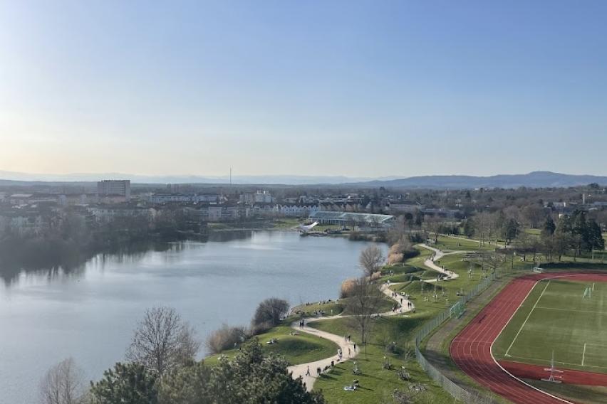 The sun is shining on Seepark, a small lake. There is a running track and walking path near the lake.