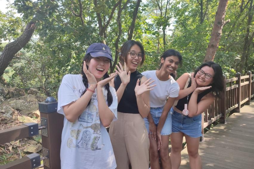 Group of female students smiling on a bridge surrounded by green trees 