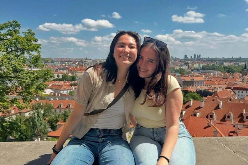 Two students seating on a wall and with a beautiful city view of Vienna in the background
