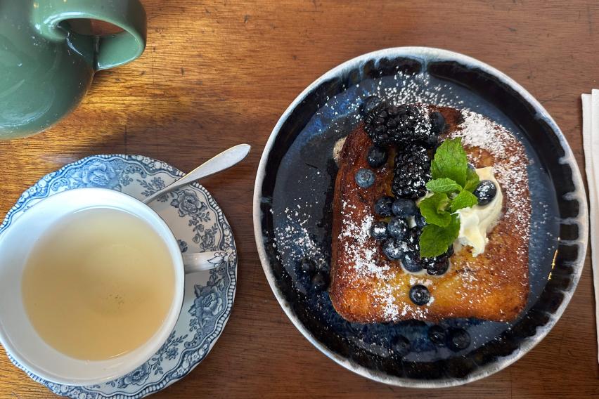 Image shows a cup of tea and a piece of french toast on a plate. The two items are next to each other.