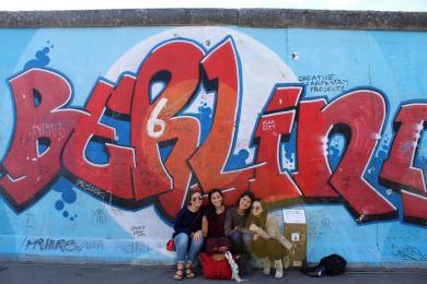 a group of students pose for a photo in front of a Berlin mural on the Berlin Wall