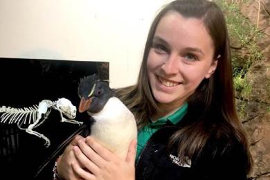 a student intern poses for a photo with a penguin at her internship
