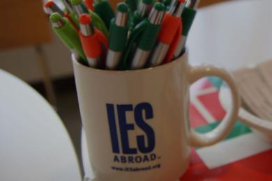 table decorated with flags, an IES branded coffee mug full of pens sits on top of it