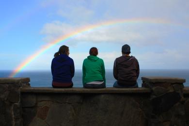 students sitting by the sea in Australia with a rainbow over them