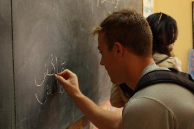 a student writing in Arabic on a chalkboard