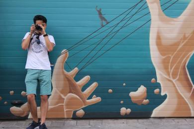 a student standing against a mural taking a photo