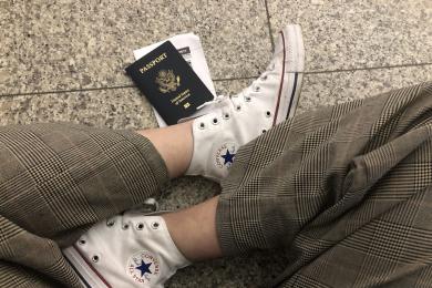 Student sits crosslegged with their passport and boarding pass in an airport