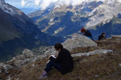 A students writes in their notebook on the side of a mountain.