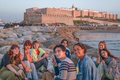 a group of students sitting near the beach with Rabat city in the background