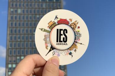 A hand holds up a sticker with the IES Abroad logo on it.