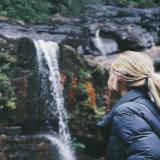 student wearing cold weather gear looking up towards a waterfall