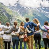 A group of students facing away from the viewer, with arms across each others shoulders staring at the sky and mountain range.