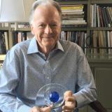 Oscar-Nominated Screenwriter Willard Huyck sitting in front of the bookshelf 
