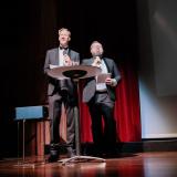 Two men stand behind a podium on a stage