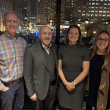 Two men and two women stand side by side in front of night skyline