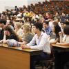 Students fill the first several rows of a lecture hall, listening to the speaker at the front of the room.