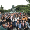 A group of students pose in front of a Buddha statue in Tokyo that has been oxidized from a gold to green color.