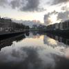 A cloudy sunrise is reflected in the River Liffey, viewed from a bridge.