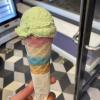 A hand holding an ice cream cone with a mint ice cream scoop on top -- the cone is pink, white, and blue-sprinkled in its top third, like the transgender flag.