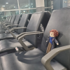 A small doll that looks like Benedict Cumberbatch's "Sherlock" sitting in the airport seats.